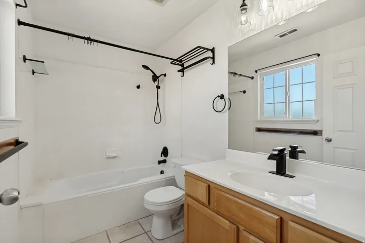 Bathroom featuring a single vanity with wood cabinetry and a white countertop, a bathtub with an integrated shower, a window with grid panes, and matte black fixtures