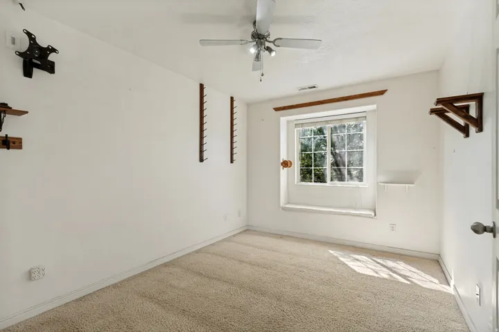 Carpeted room featuring a ceiling fan with integrated lighting, a window with a sill, and built-in wall shelving