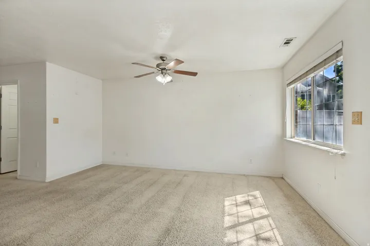 Spacious room with plush carpeting, a large window, and a ceiling fan