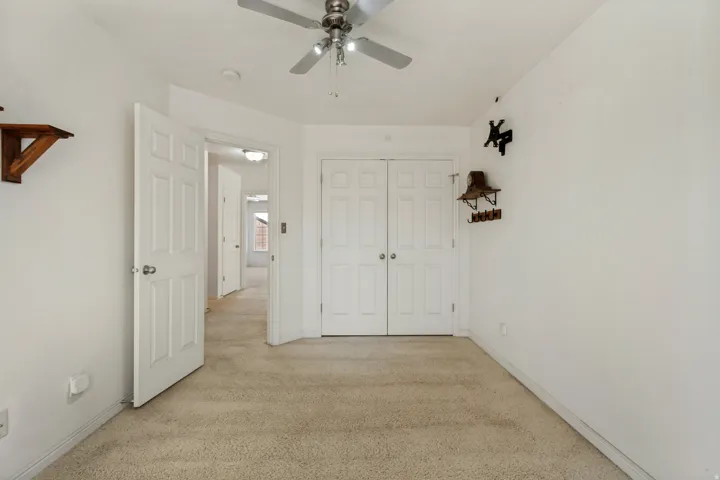 Neutral-toned carpeting, ceiling fan with integrated lighting, and white paneled doors