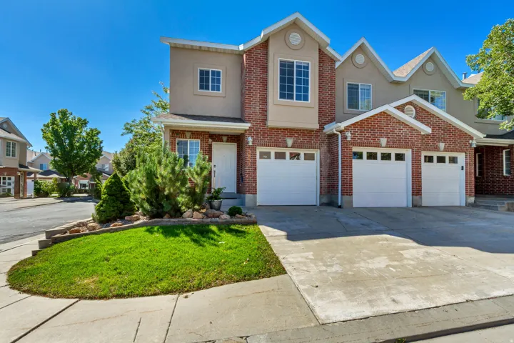 Brick and stucco exterior with multiple gables, a multi-car garage, concrete driveway, and established front landscaping
