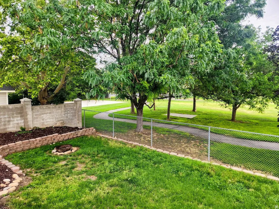 Expansive outdoor space featuring a manicured lawn, established trees, and a paved pathway