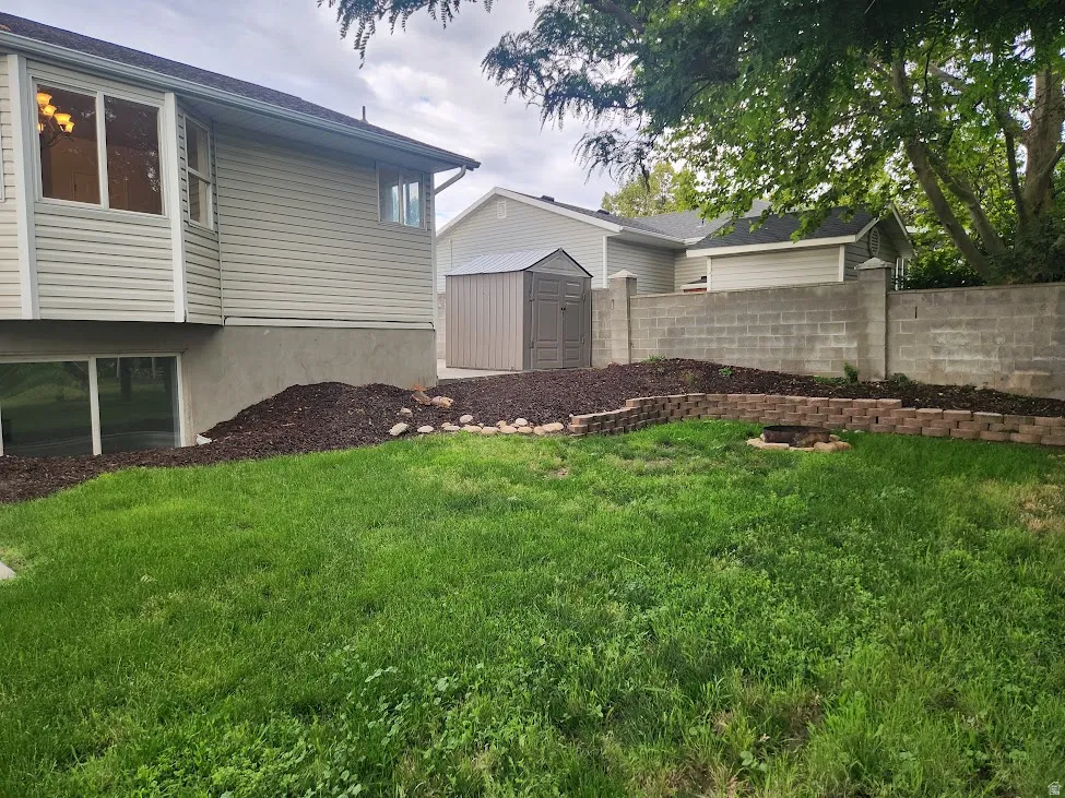 Manicured lawn with a tiered retaining wall, concrete block privacy wall, and a built-in fire pit