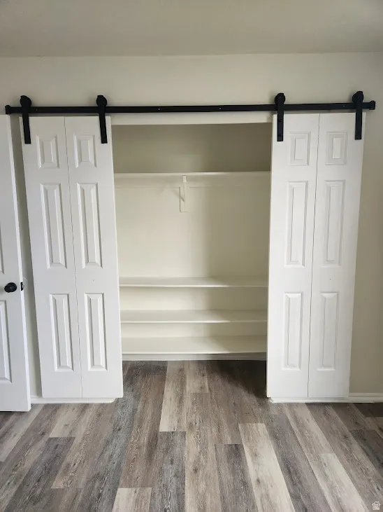 Barn door style closet doors with black hardware, built-in shelving, and wood-finish flooring