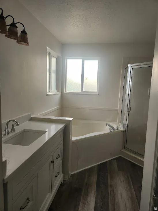 Wood-finish flooring, white vanity with integrated sink, light countertop, built-in tub, and glass-enclosed shower
