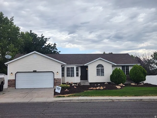 Single-story residence featuring light-toned siding, an attached two-car garage, and a landscaped front yard with decorative rocks and shrubbery