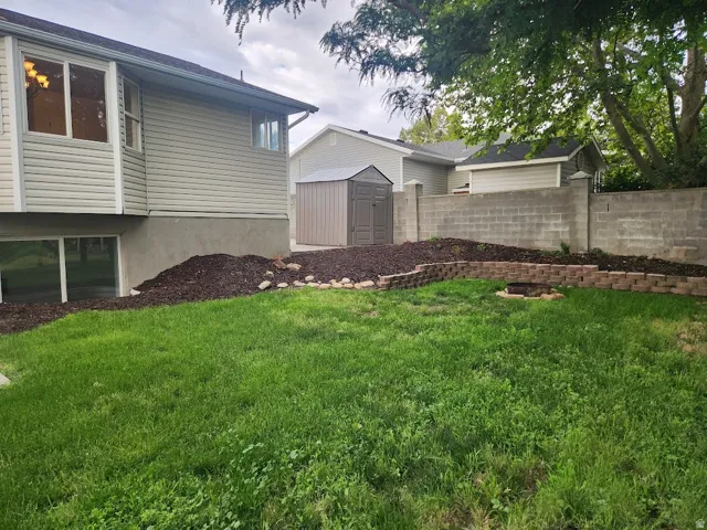Manicured lawn with a tiered retaining wall, concrete block privacy wall, and a built-in fire pit