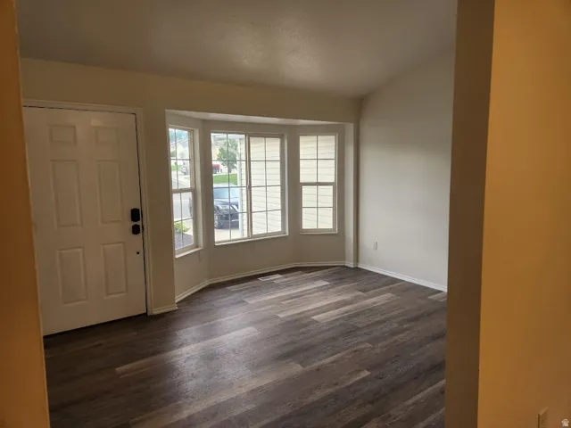 Wood-finish flooring, bay window, white paneled entry door, and vaulted ceiling