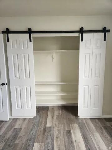 Barn door style closet doors with black hardware, built-in shelving, and wood-finish flooring