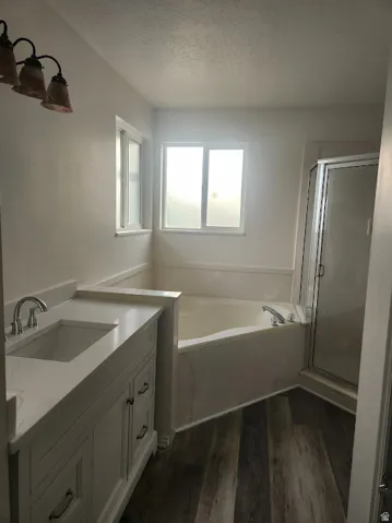 Wood-finish flooring, white vanity with integrated sink, light countertop, built-in tub, and glass-enclosed shower