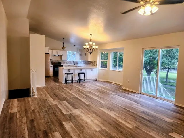 Vaulted ceilings, wood-finish flooring, white cabinetry, a kitchen island with seating, and a sliding glass door to exterior
