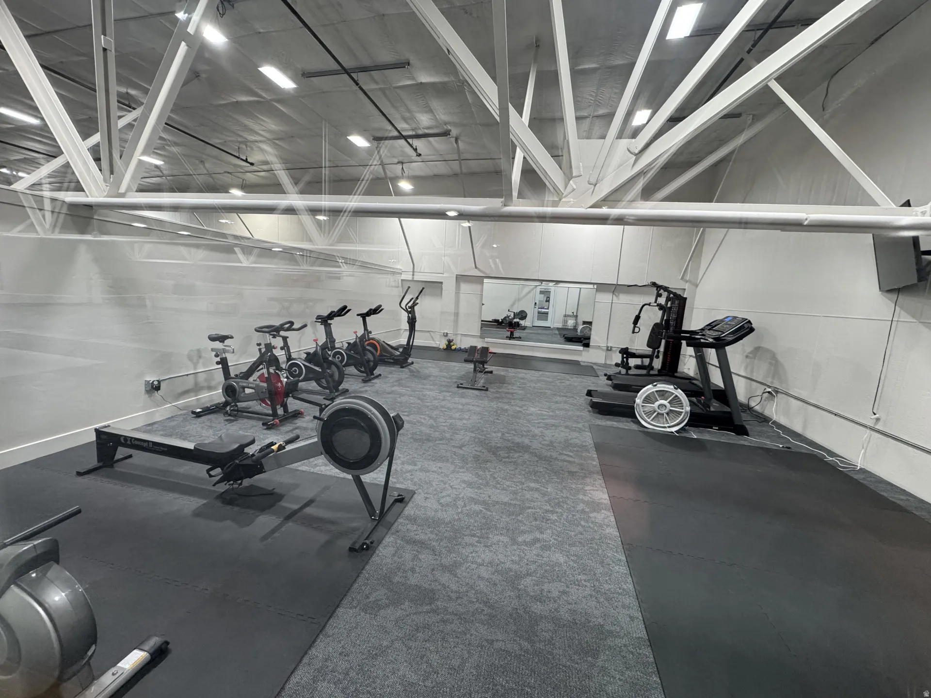 Spacious fitness area featuring high ceilings with exposed trusses, a mirrored wall, and specialized rubber and carpet flooring