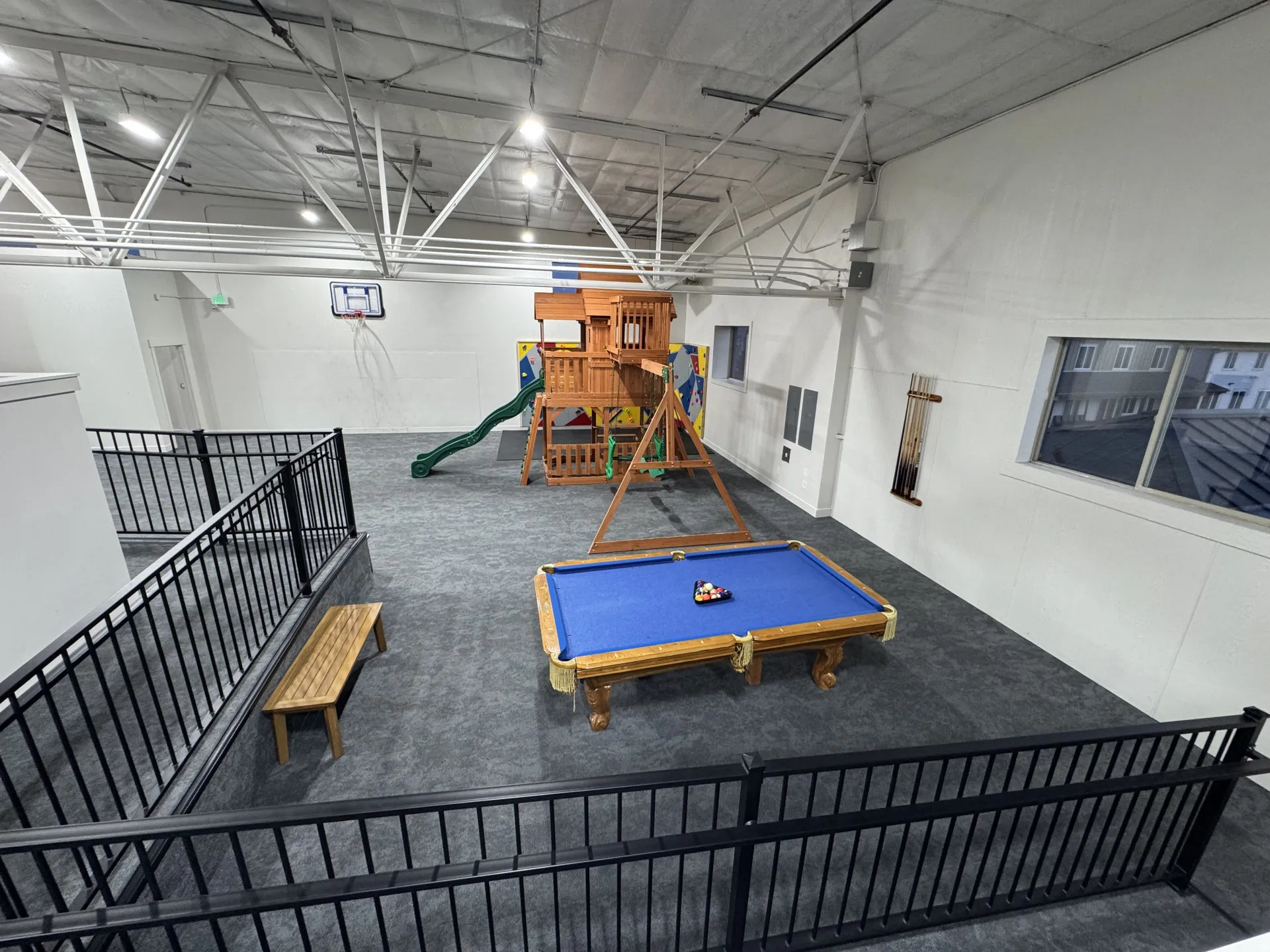 Spacious recreational area featuring high ceilings, exposed trusses, multiple windows, and a built-in play structure