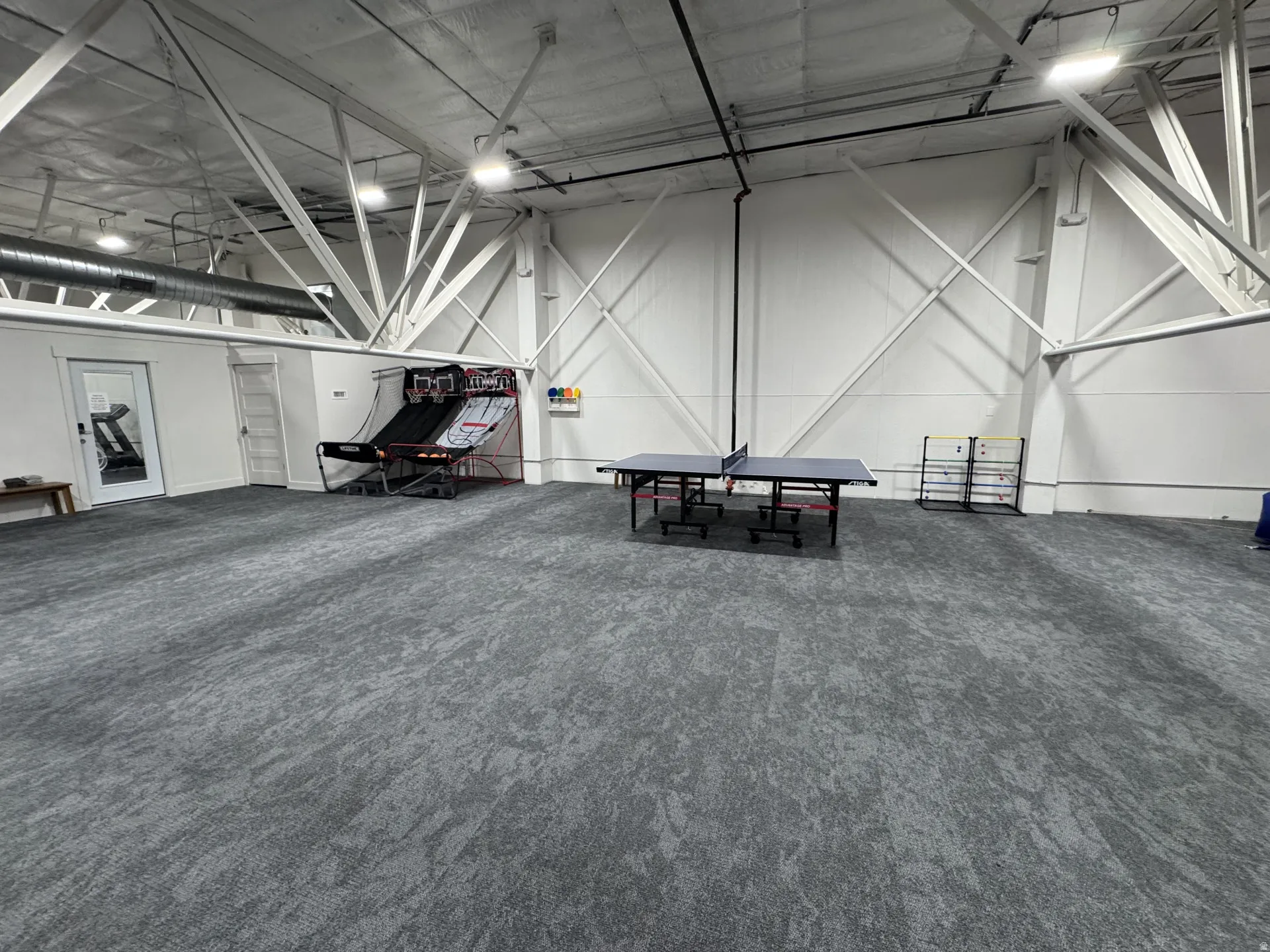 Spacious open area featuring gray patterned carpeting, exposed white structural beams, and integrated ceiling lighting