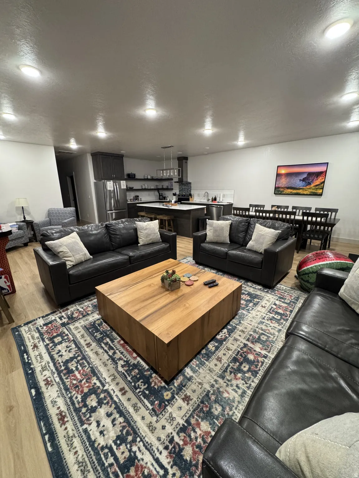 Open-concept living area with wood-finish flooring, recessed lighting, and a kitchen featuring dark cabinetry