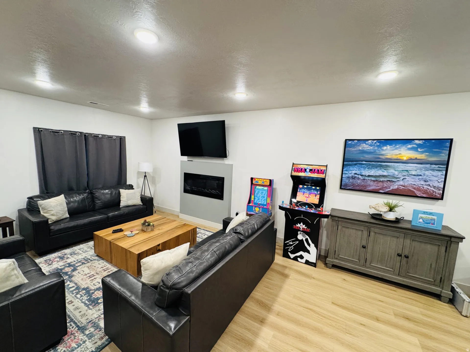 Recessed lighting, wood-finish flooring, electric fireplace, built-in media console, and window with dark drapery
