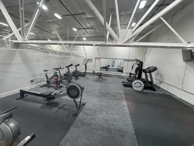Spacious fitness area featuring high ceilings with exposed trusses, a mirrored wall, and specialized rubber and carpet flooring