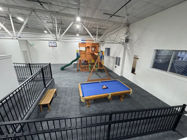 Spacious recreational area featuring high ceilings, exposed trusses, multiple windows, and a built-in play structure