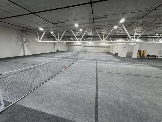Indoor court space featuring multiple playing areas, high ceilings with exposed trusses, and integrated overhead lighting