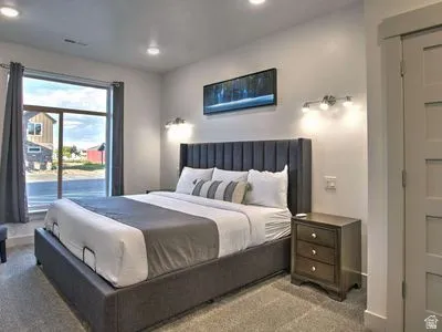 Recessed ceiling lighting, large window with roller shades, wall-mounted sconces, and panel-style door