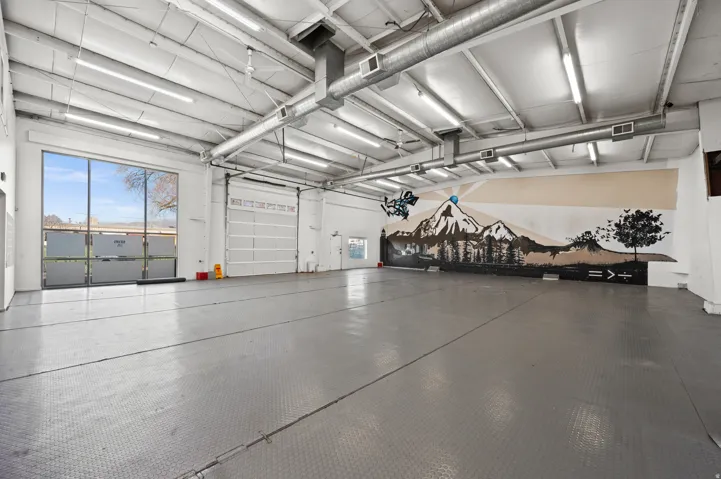 Expansive open interior with high ceilings, recessed lighting, polished concrete flooring, two large roll-up doors, and a full-height window wall