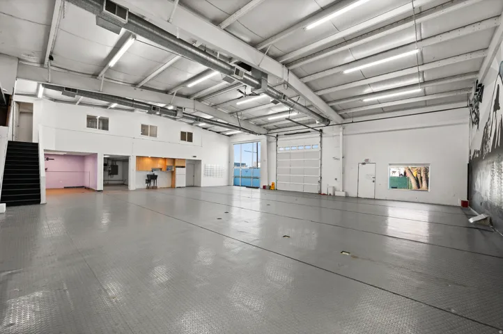 Expansive open floor plan with high ceilings, polished concrete flooring, a roll-up garage door, and a built-in kitchenette
