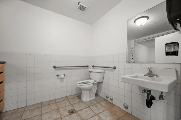 White tile wainscoting with accent trim, pedestal sink, wall-mounted mirror, and tile flooring