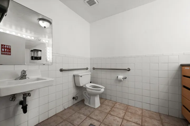 White tiled walls, a white toilet, and a white sink with a chrome faucet