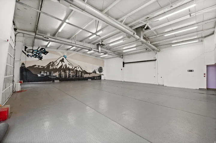 Spacious interior with high ceilings, exposed ductwork, fluorescent lighting, and a roll-up garage door