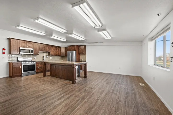 Open-concept living space featuring wood-finish flooring, a full kitchen with stainless steel appliances, and abundant natural light from the window