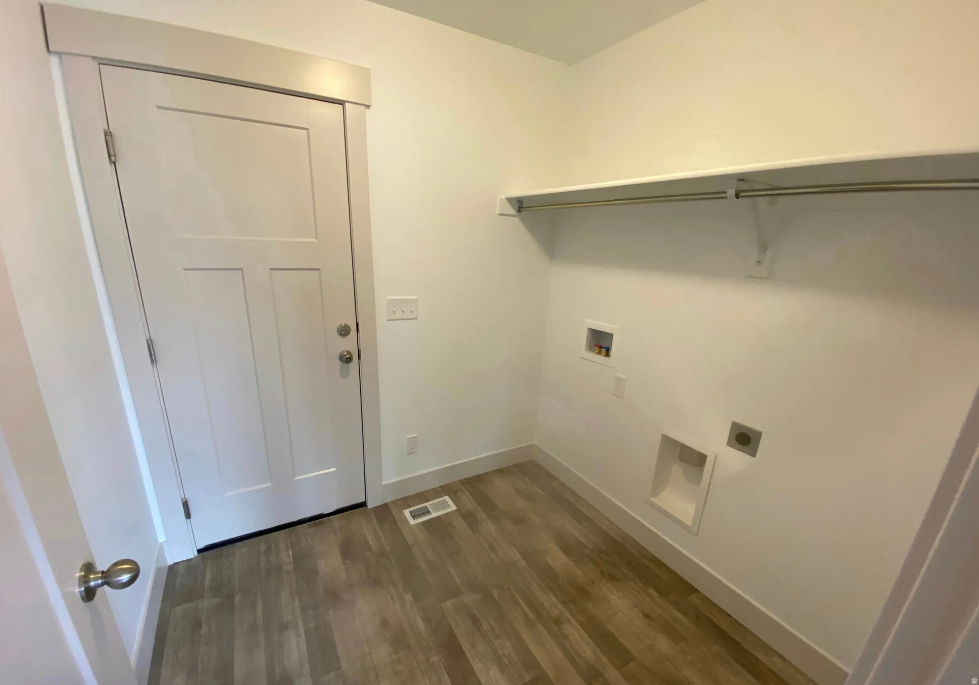 Laundry area with wood-finish flooring, white walls, and a built-in shelf with hanging rod