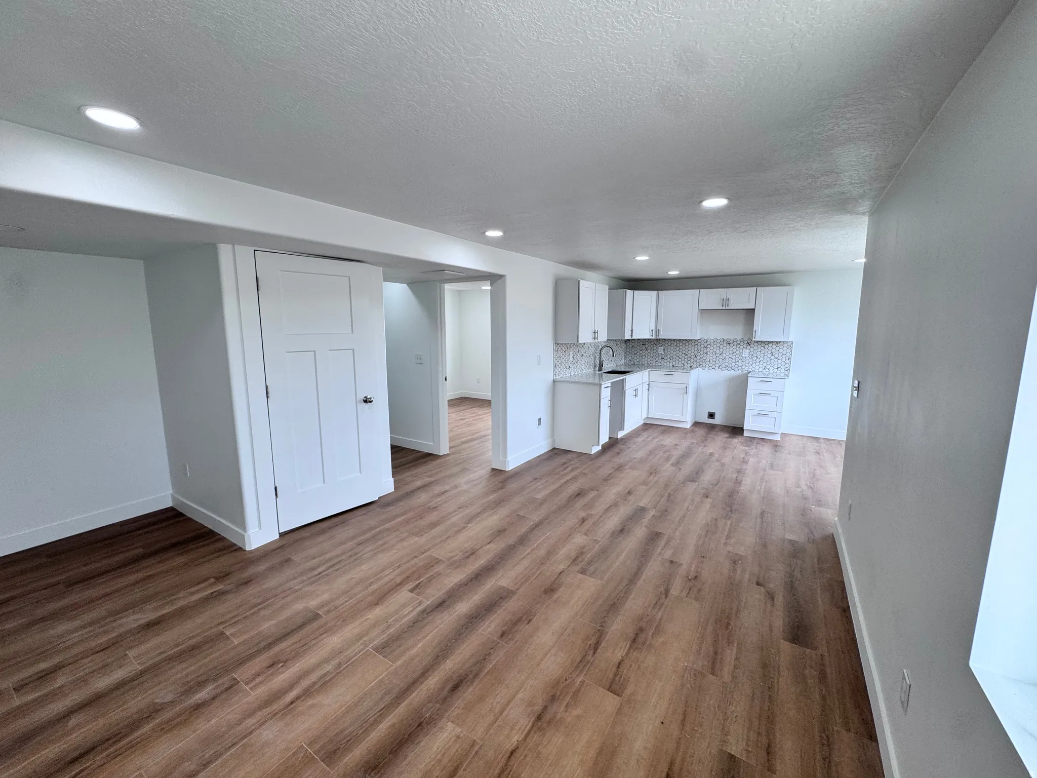 Open-concept living space with wood-finish flooring, white cabinetry, a tiled backsplash, recessed lighting, and white interior doors