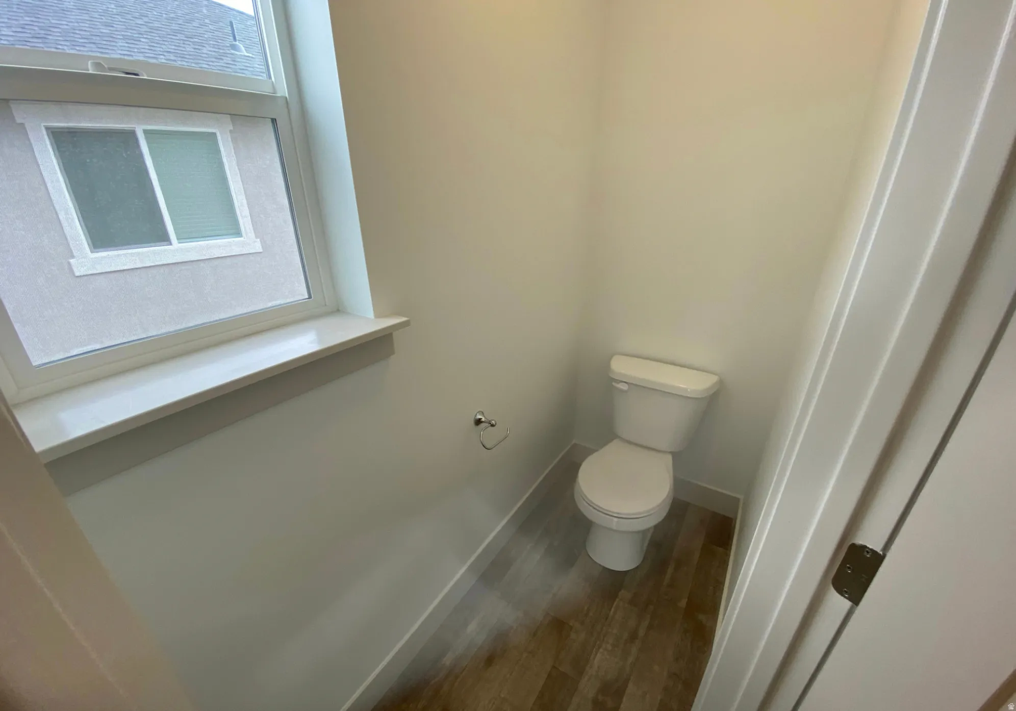 Contemporary water closet with a white toilet, wood-finish flooring, and a white window frame with a sill