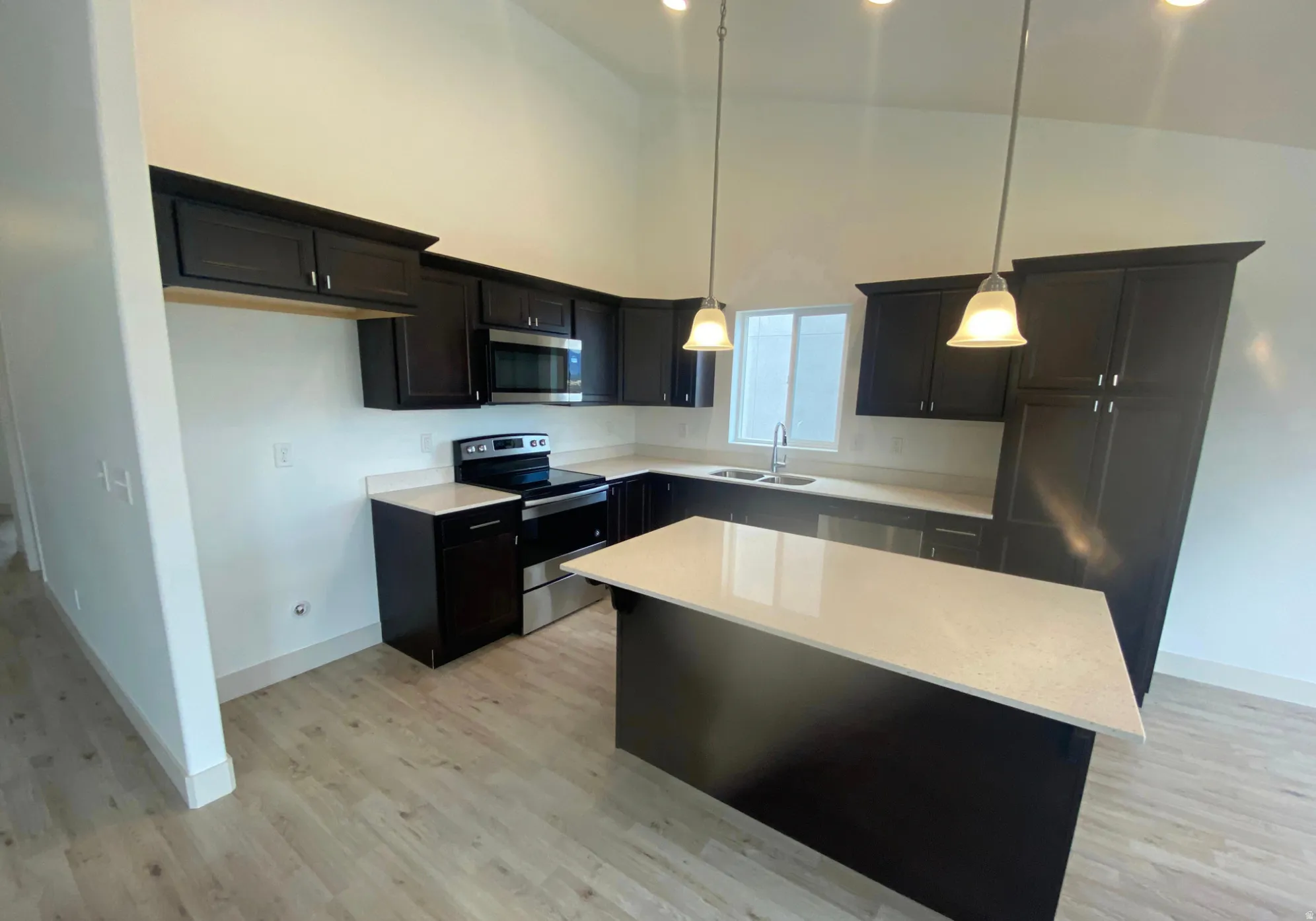 Kitchen featuring vaulted ceilings, dark wood cabinetry, light-toned countertops, stainless steel appliances, and wood-finish flooring