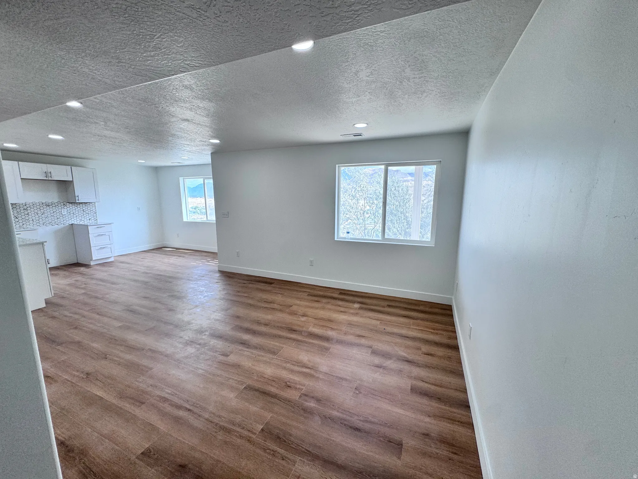 Recessed lighting, wood-finish flooring, white cabinetry, light-toned backsplash, and a window with a mountain backdrop