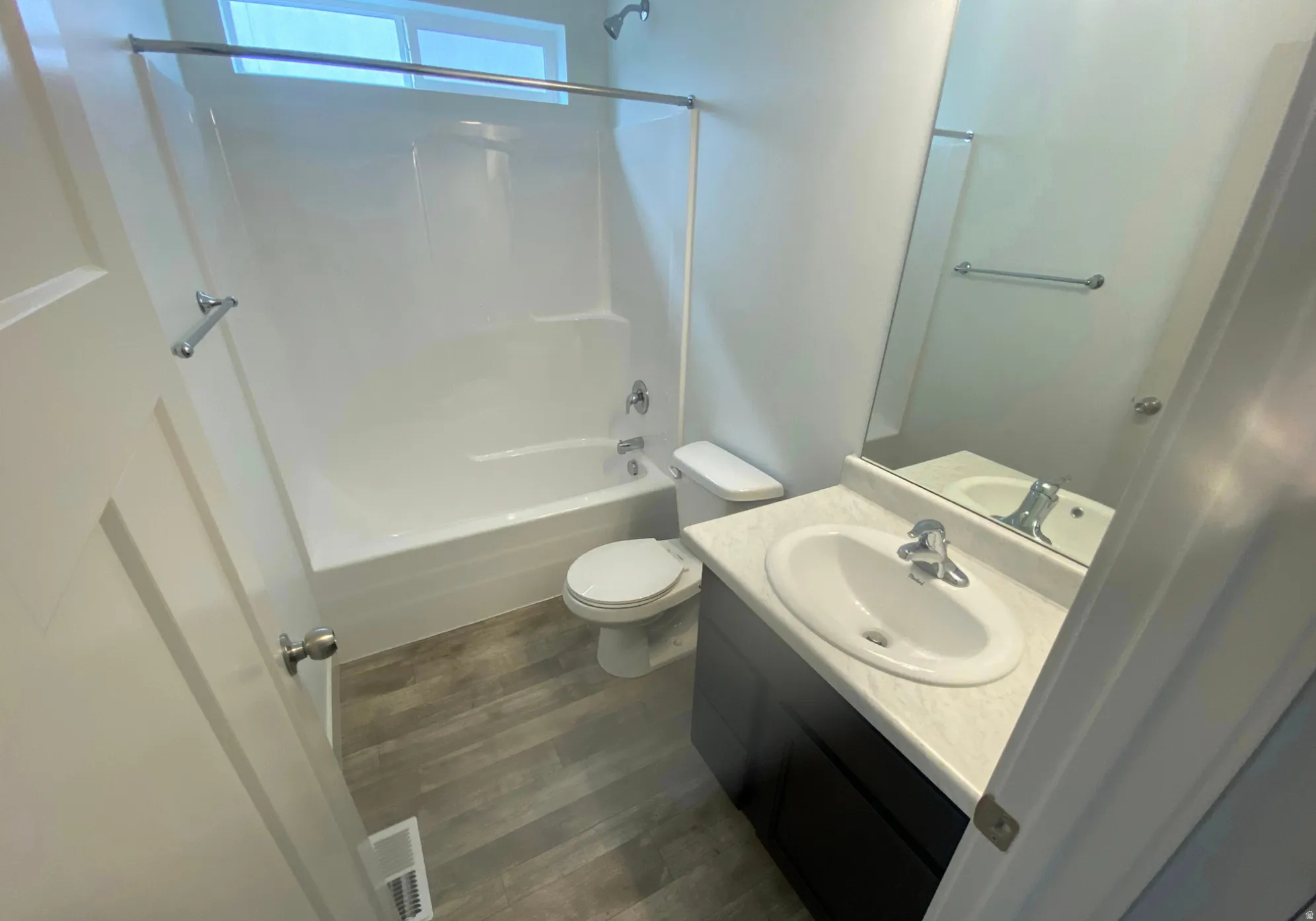 Contemporary bathroom featuring a white tub/shower combination, dark wood-finish vanity with an integrated sink, and wood-finish flooring