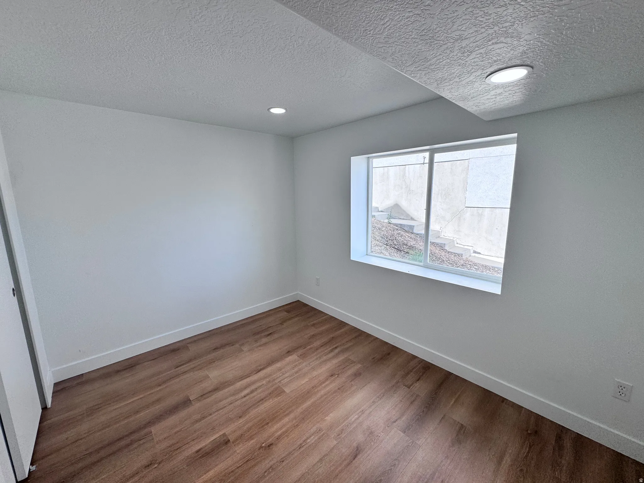 Wood-finish flooring, recessed lighting, base molding, and a window with a white frame