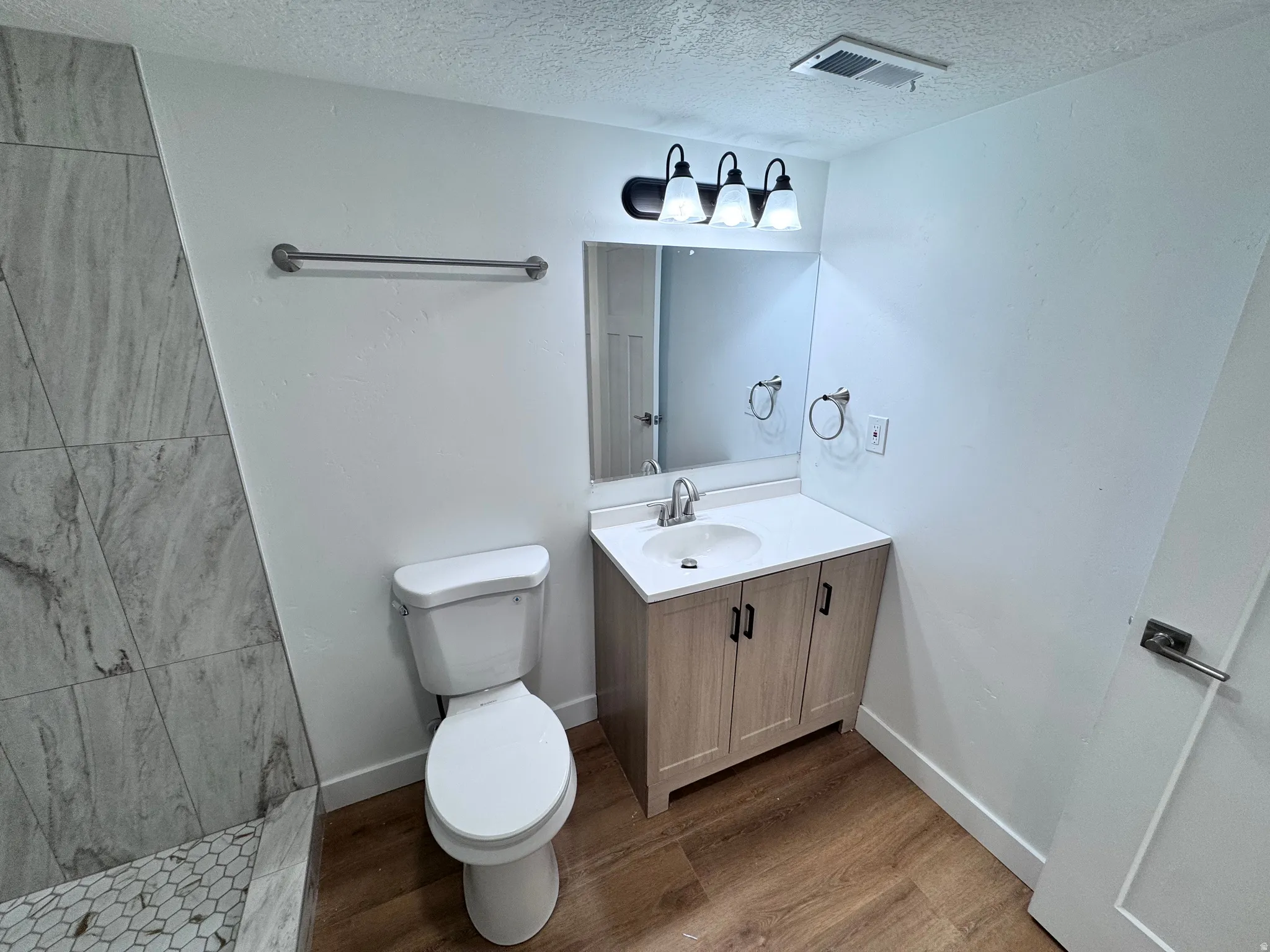 Wood-finish flooring, white vanity with matte black hardware, white countertop, and light-toned wall tile