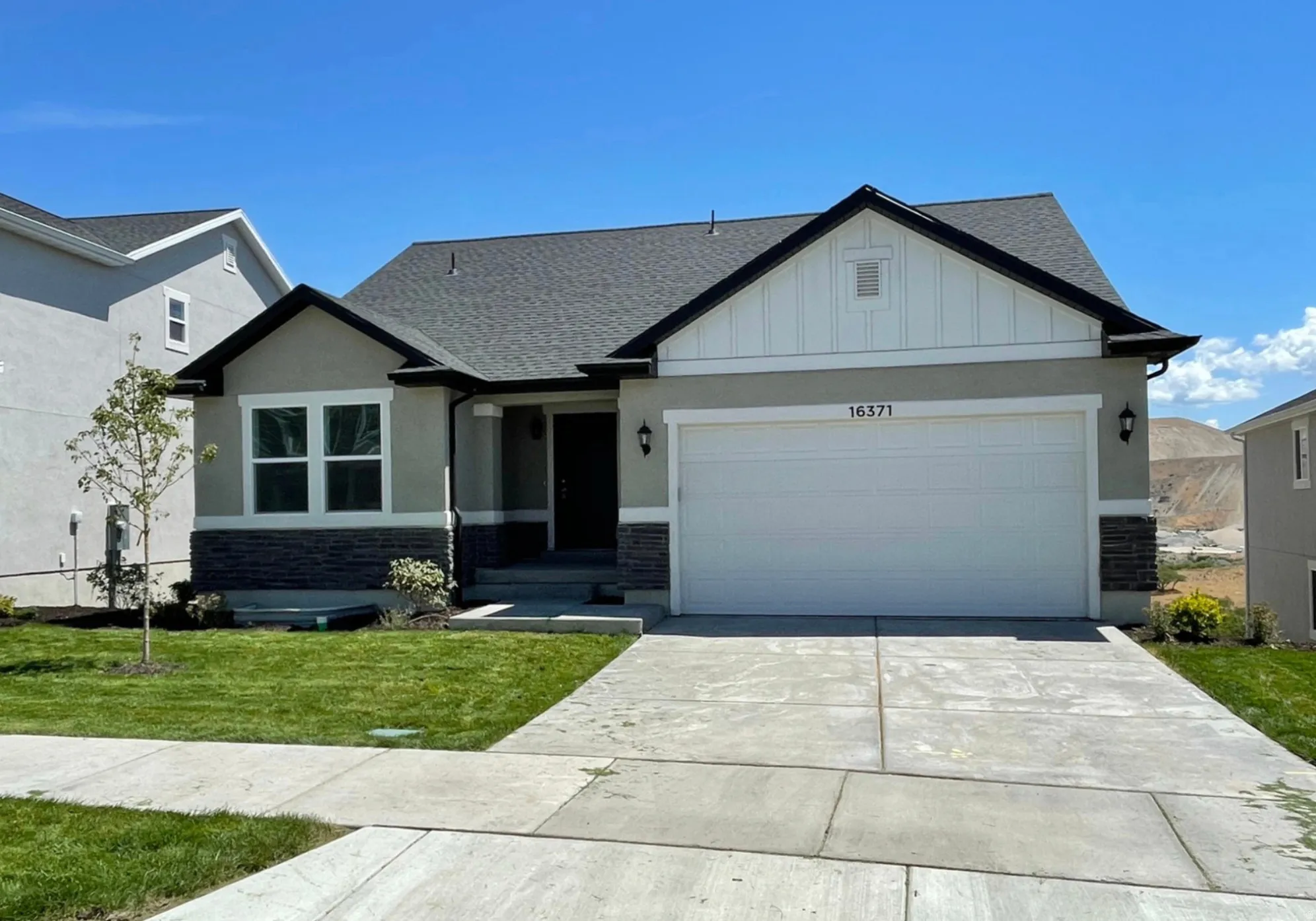 Single-story residence featuring a two-car garage, gray shingle roof, stone veneer accents, and a concrete driveway