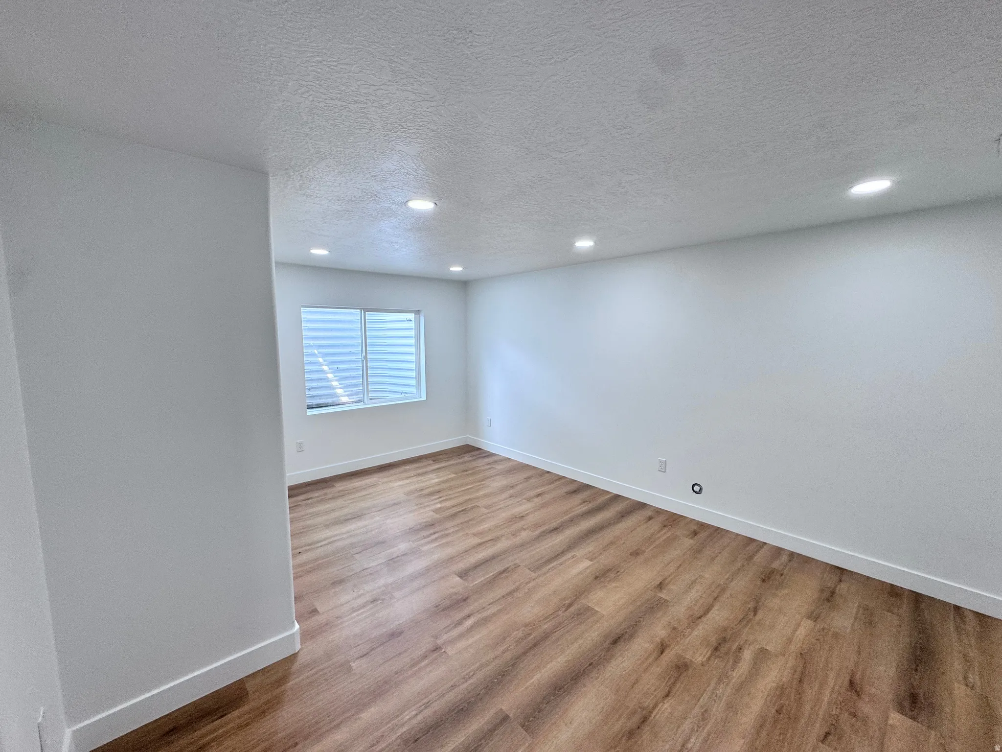 Recessed lighting, wood-finish flooring, white walls, and a window with horizontal blinds
