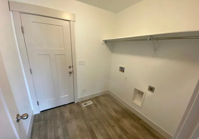 Laundry area with wood-finish flooring, white walls, and a built-in shelf with hanging rod