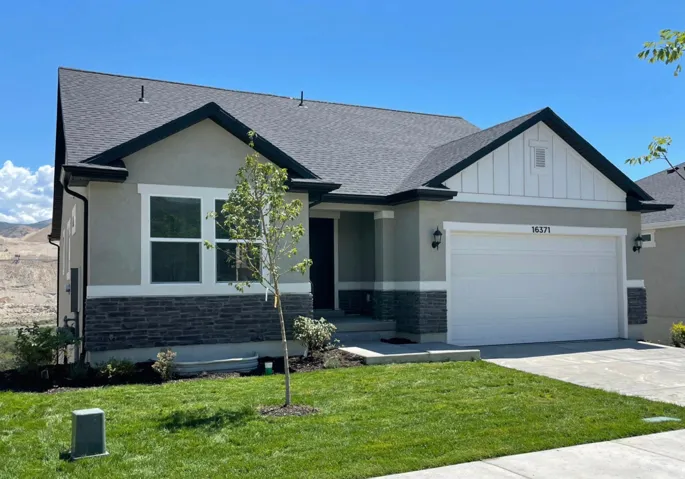 Stucco exterior with stone accent, white garage door, dark shingle roof, and manicured lawn