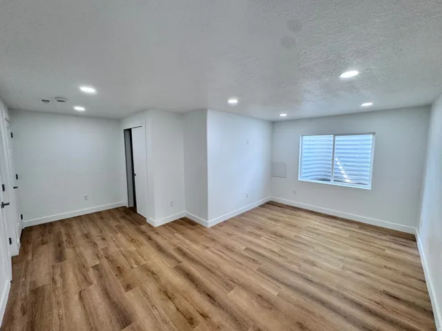 Bright, open living space featuring recessed ceiling lighting, wood-finish flooring throughout, and large windows with plantation shutters providing natural illumination