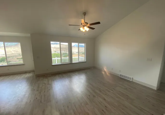 Vaulted ceiling with a ceiling fan, multiple windows with a mountain backdrop, and wood-finish flooring