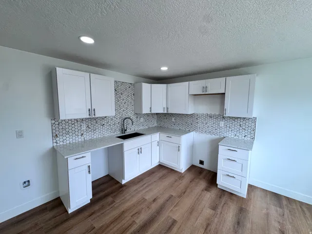 White shaker-style cabinetry with matte black hardware, hexagonal tile backsplash, light-toned countertops, and wood-finish flooring