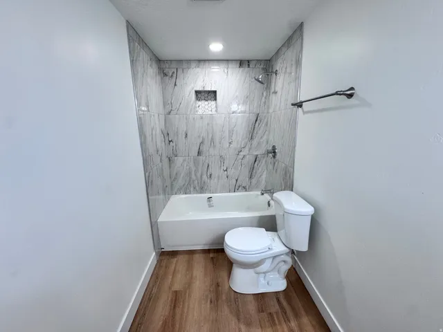 Bathtub with a shower featuring marble-look wall tiling and a tiled shower niche