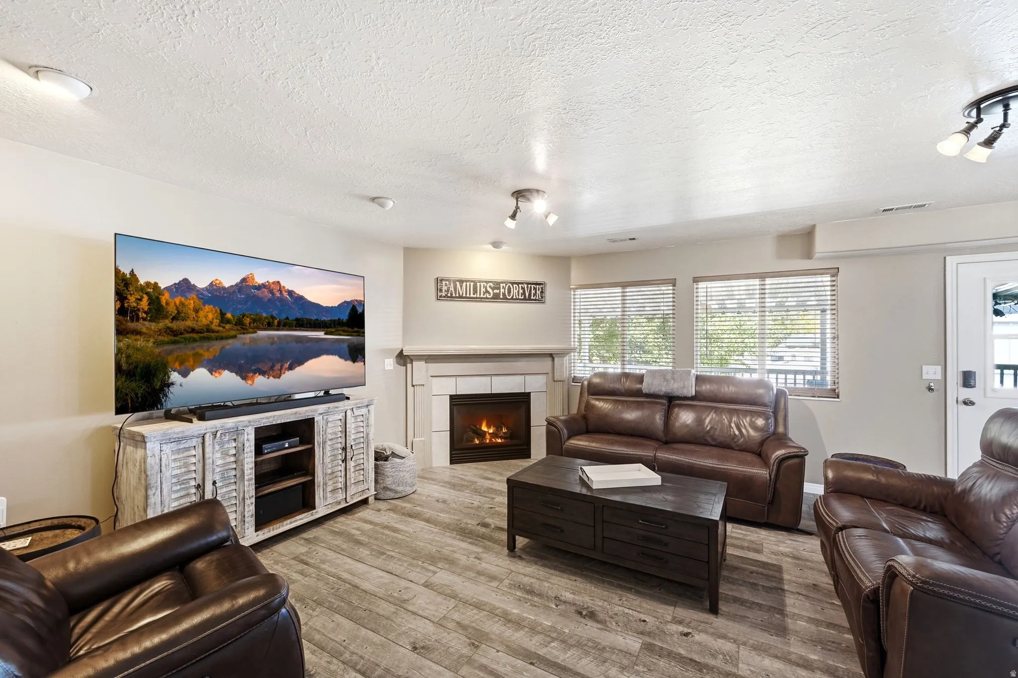 Living space featuring wood-finish flooring, a fireplace with a mantel, multiple windows with blinds, and recessed lighting