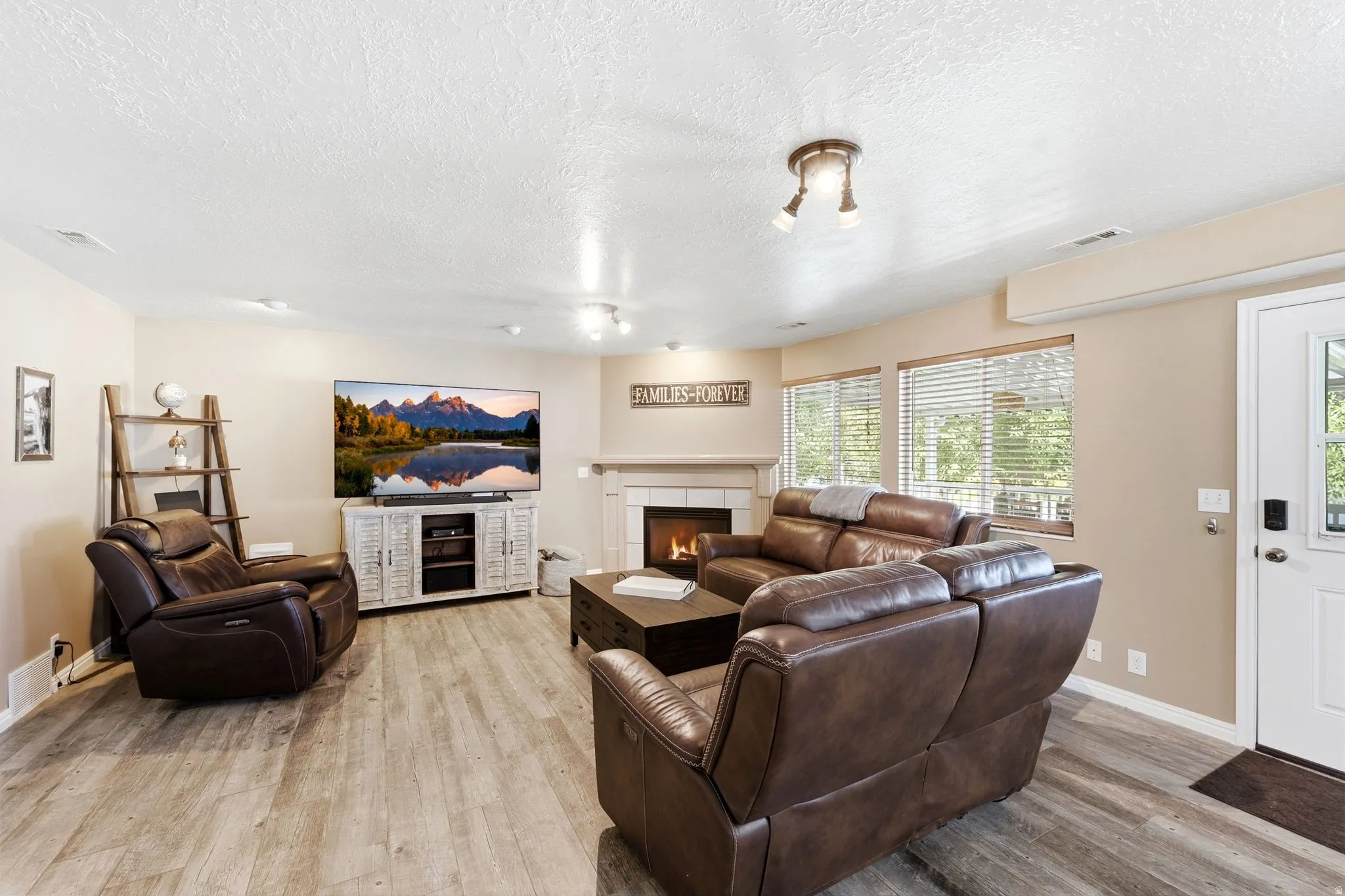 Spacious living area featuring wood-finish flooring, a fireplace with a mantel, multiple windows with blinds, and recessed lighting
