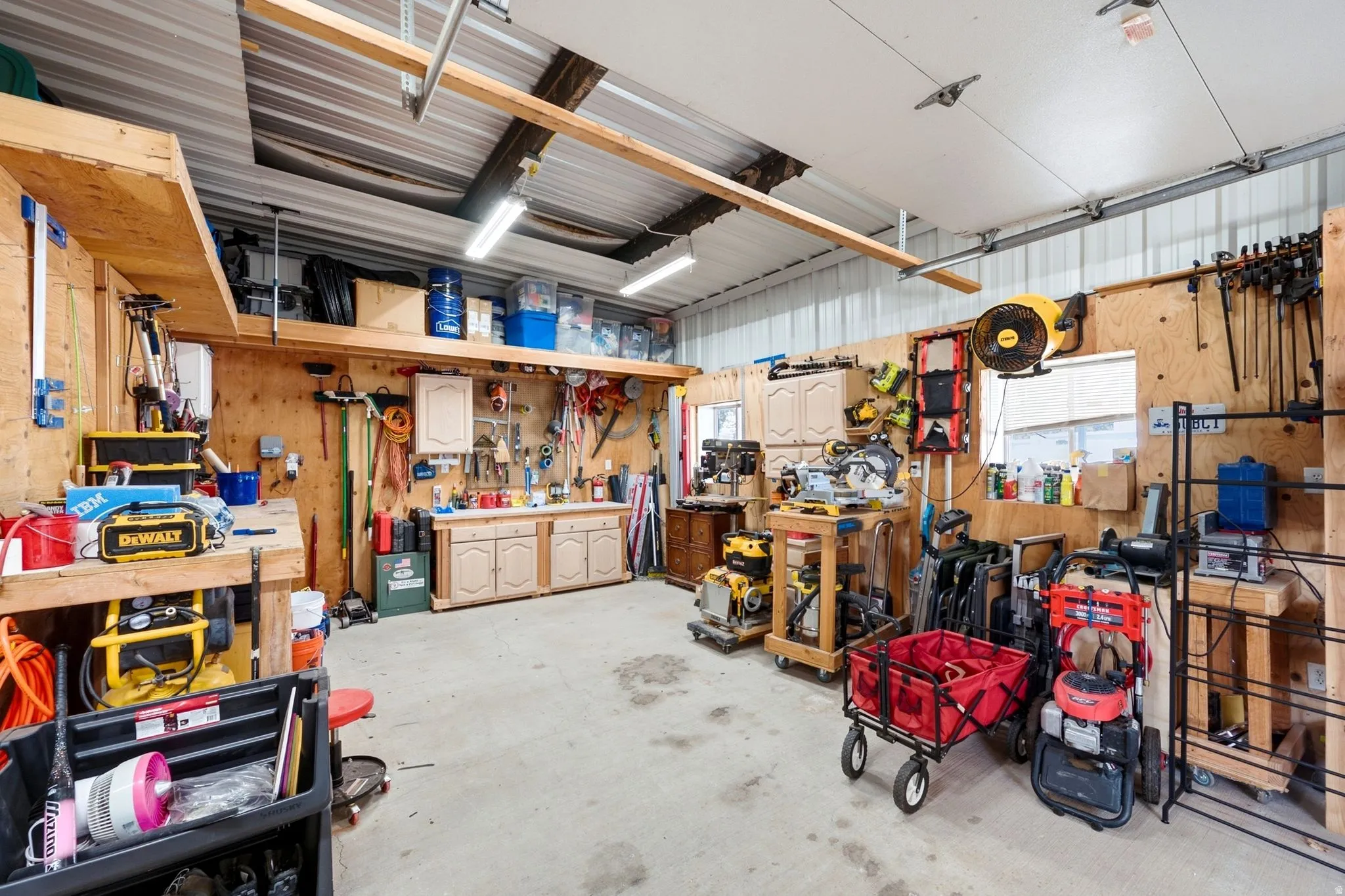 Spacious utility area featuring exposed wood walls, built-in shelving, mounted cabinetry, and concrete flooring