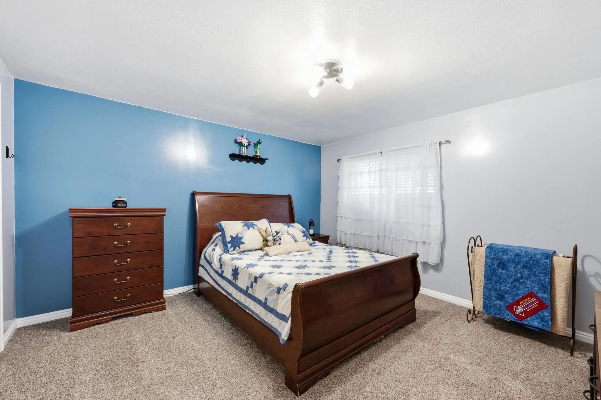 Carpeted room featuring a ceiling-mounted light fixture and window with white window treatments
